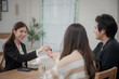 © surachetkhamsuk - Estate agent hands house keys to the client. Asian woman realtor gives keys to the couple buyer while sitting at a table with a house model. Real estate