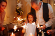 © Halfpoint - Grandparents and granddaughter holding sparklers during Christmas celebration.