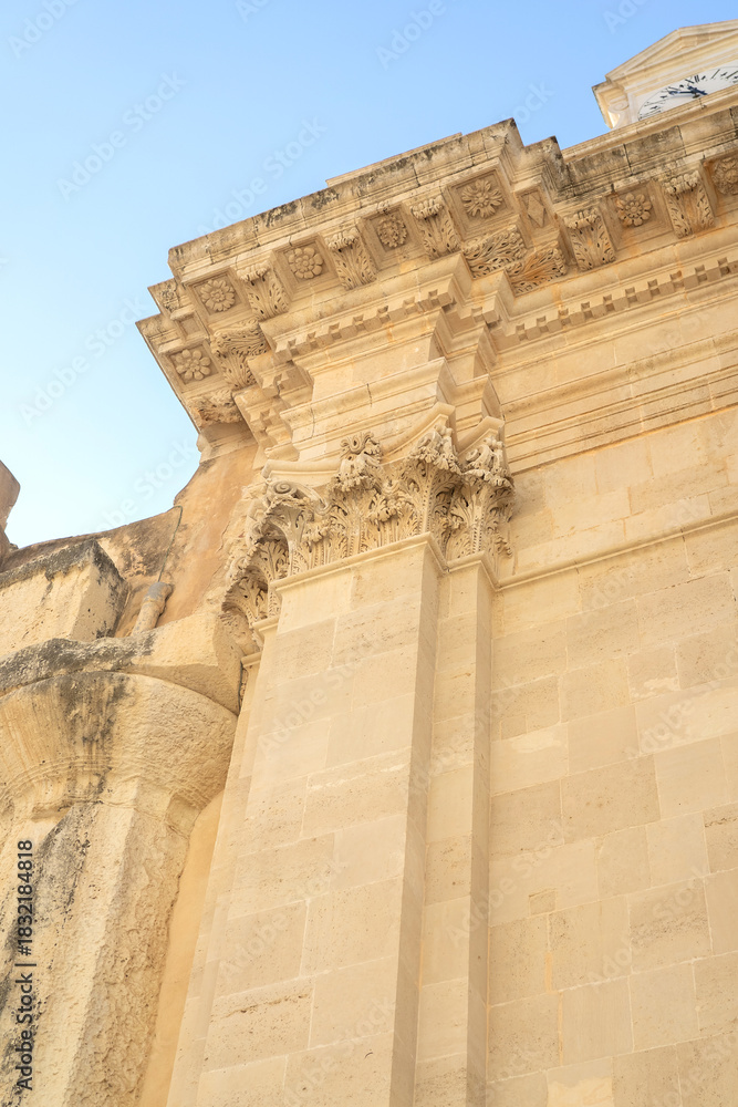 detailed photograph showcasing the ancient stone exterior of the Cathedral of Syracuse (Cattedrale di Siracusa) in Sicily. The image highlights the weathered limestone walls, historic architectural