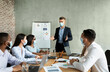 © Prostock-studio - Businessmen and women in masks gather in a modern office to discuss company strategy. A young CEO leads the meeting, presenting ideas to diverse coworkers.