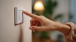 © imagemir - A close-up of a woman's hand, gently pressing a light switch in a cozy, softly lit room.