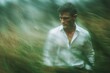 © MdHafizur - a handsome man in a white shirt, walking through waves of green grass, with a blurred background and a large aperture.