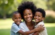 © li - Portrait of smiling black woman embracing two sons at family gathering outdoors, copy space. High quality
