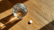 © Tap - Glass of water and one white pill on wooden table