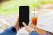 © Kunlathida - Female hand holds modern smartphone with blank screen. Background blurred with cup of ice tea