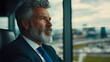 © sommersby - Successful mature businessman with grey beard in suit looking reflectively out of high-rise office window at city skyline, contemplating future strategies and leadership