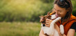 © kathrineva20 - Woman Kissing Border Collie Puppy Outdoors. Smiling woman in an orange vest holds her Border Collie puppy in her arms while the dog licks her face in a sunny green park.