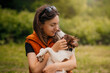 © kathrineva20 - Woman Holding Border Collie Puppy in Park. Young woman in an orange vest gently hugs her Border Collie puppy while the dog nuzzles her face in a green park.