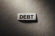 © Win Nondakowit - word “DEBT” on a textured paper surface with dramatic lighting. Dark shadows convey financial stress, economic burden, and money problems.