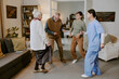 © AnnaStills - Group of two senior Caucasian women, senior Caucasian man and young adult Hispanic woman laughing and dancing together in living room, nurse wearing medical scrubs joining activity