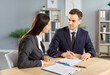 © Studio Romantic - Two confident business people man and woman at work in office. Young company employees sitting at the desk with documents on workplace having discussion and going to sign a contract.