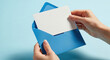 © smth.design - Hands holding blank white card and opening blue envelope against pastel background for message, invitation or announcement concept