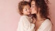 © fotofabrika - Mother kisses daughter in cozy space with soft pink background