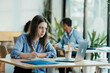 © Suteren Studio - Female Student Taking Notes from Online Lecture in Sunny University Cafeteria During Lunch