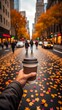 © NoorArt Studio - Hand holding coffee cup on city street with autumn leaves