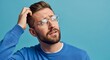 © Mostafizur - Confused young man in glasses and blue sweater scratching his head while looking up, posing against a blue background