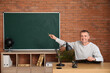 © Pixel-Shot - Male teacher with clipboard sitting at table in classroom and conducting lesson