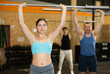 © JackF - Motivated young woman practicing exercises with rod near other people in gym