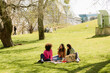 © Drobot Dean - A woman is eating and sitting on a blanket next to two female friends who are looking at her