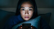 © Nai - Person looks at smartphone while sitting on bed at night in dark room using soft light to read messages or browse content