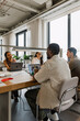 © Drobot Dean - A group of four employees are sitting at a table while two of them are in front of laptops and one of them is smiling and reading a document