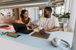 © Drobot Dean - A male employee is talking to a female employee who is sitting next to him at the desk and holding a pen while listening