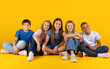 © Anastasiya - Smiling preteen kids sitting together on the floor on bright yellow studio background. A friendly group of children showing closeness, comfort and a relaxed school lifestyle scene