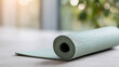 © Anastasiya Marchenko - Close-up of a rolled light green yoga mat on a smooth surface with soft natural light and blurred background