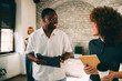 © djile - Smiling diverse colleagues, an African American man and a caucasian woman, have a relaxed and engaged discussion during a break in the office