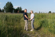 © Irina - Elderly couple stands face to face in a grassy meadow, holding hands and smiling on a clear summer day