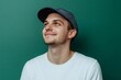 © Татьяна Евдокимова - Happy young man in white tee and baseball cap smiling and looking up to blank green space, hopeful and confident headshot