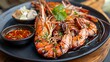 © RanaMuhammad - Grilled river prawns served on a black plate with dipping sauce and garnish on a wooden surface