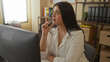 © Krakenimages.com - Woman sitting in modern office working on computer with thoughtful expression surrounded by shelves books and potted plants in a comfortable indoor setting.