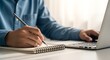 © Zamans - Person Writing Notes While Using Laptop Computer.
