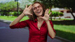© Krakenimages.com - Woman smiling in red shirt with glasses in sunny park, surrounded by greenery, embodying joy and outdoor leisure.