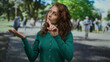 © Krakenimages.com - Woman in green sweater on city street with hand gesture, surrounded by blurred outdoor background and people, stands with closed eyes, depicting casual urban scene.