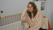 © Krakenimages.com - Woman sitting tired in bedroom with baby crib nearby in cozy home interior wearing sweater with closed eyes indoors.