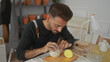 © Krakenimages.com - Young man wearing apron kneads clay on wooden table in studio beside sculpting tools; craftsmanship concentration.