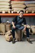 © Artem Varnitsin - Exhausted warehouse worker sitting on a coffee bag and looking at camera. Young worker in apron sitting in warehouse.