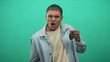 © Krakenimages.com - Young hispanic man holding car keys, clenched right fist toward camera, squinting face and pursed lips, wearing denim jacket in studio green screen; defiance.
