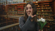 © Krakenimages.com - Young woman holding white tulips, smiling and cupping hand near mouth in library building balcony; playful joy curiosity.