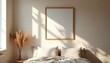 © Vadym - Modern bedroom features blank wooden frame above comfortable bed. Sunlight casts plant shadows on wall, creating serene ambiance. Pampas grass in vase adds to clean, cozy, minimalist, inviting home