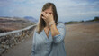 © Krakenimages.com - Young woman in light blue blouse pinches nose on street beside rocky embankment under sunlit sky; disgust.