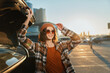 © SHOTPRIME STUDIO - Woman with sunglasses and beanie by car trunk in parking lot at sunset, plaid jacket and warm smile, candid authenticity, golden hour glow and emotional storytelling vibe.