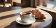 © Kabita - Coffee cup and croissant on a wooden table in soft sunlight.