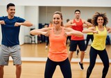 Cheerful men and women enjoying a high energy group aerobics or fitness dance class in a bright gym studio