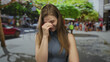 © Krakenimages.com - Woman in blue sleeveless top pinches nose on busy street lined with trees and parked cars; disgust.