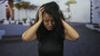© Krakenimages.com - Woman feeling stressed on a sunny outdoor street, holding head in hands, young hispanic female expressing frustration in latin urban background.