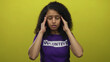 © Krakenimages.com - Woman wearing volunteer shirt stands against vibrant yellow background, appearing stressed, showcasing emotion with hands on temples.