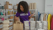© Krakenimages.com - Young woman volunteering indoors at a charity center, packing food into bags with stacked containers and clothing donations visible around the room.